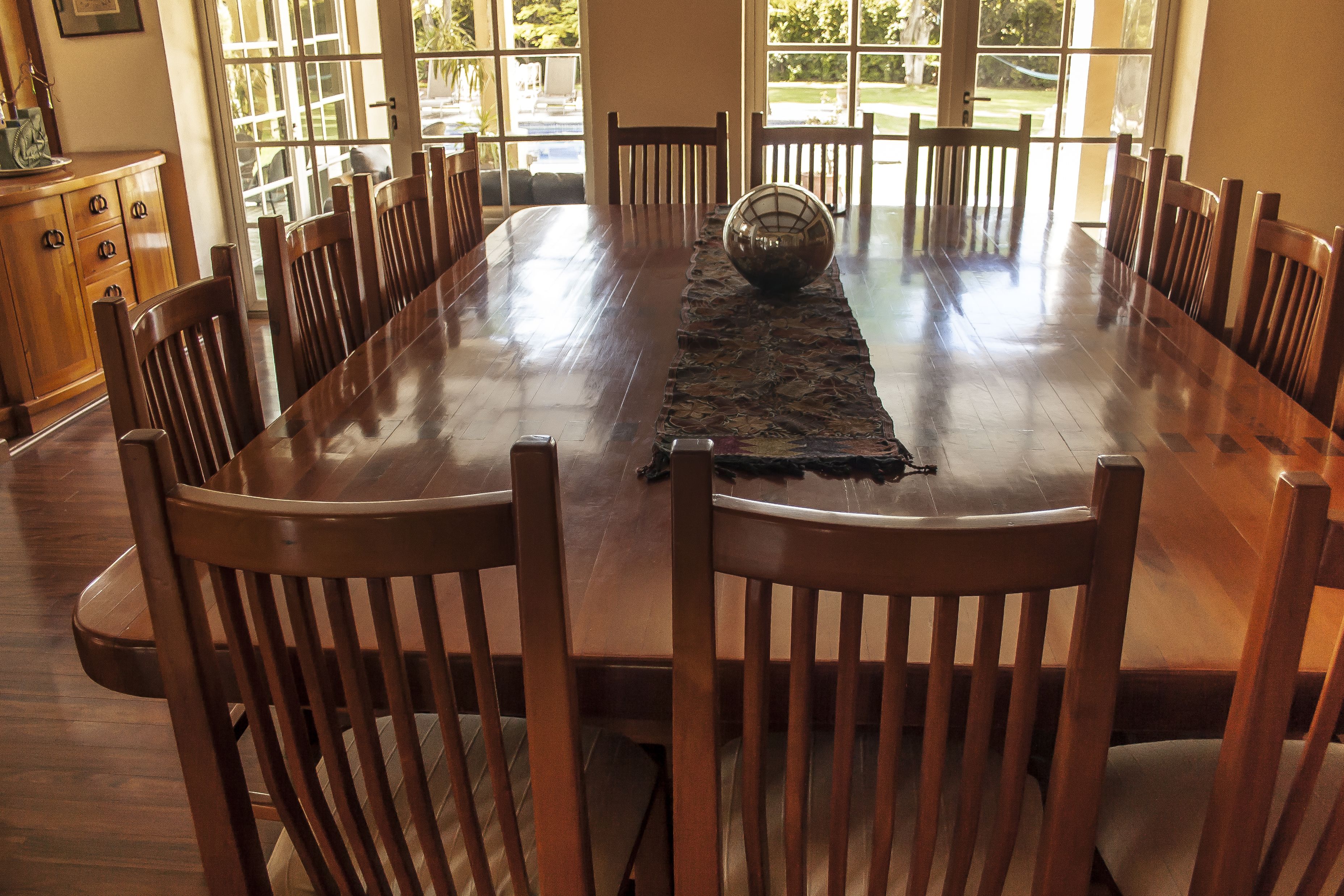 A large wooden dining table with chairs around it, a decorative glass bowl, and a view of the outdoors through large windows.