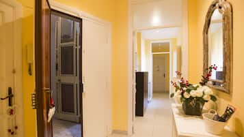 Un corridoio con una porta bianca, uno specchio e un cesto di fiori bianchi su un tavolo consolle bianco.