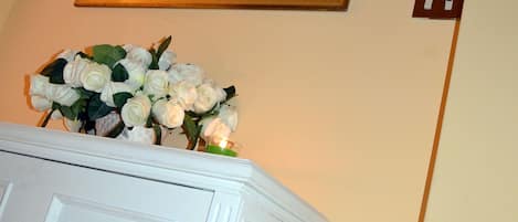 A framed painting of a coastal scene above a white cabinet with a bouquet of white flowers.