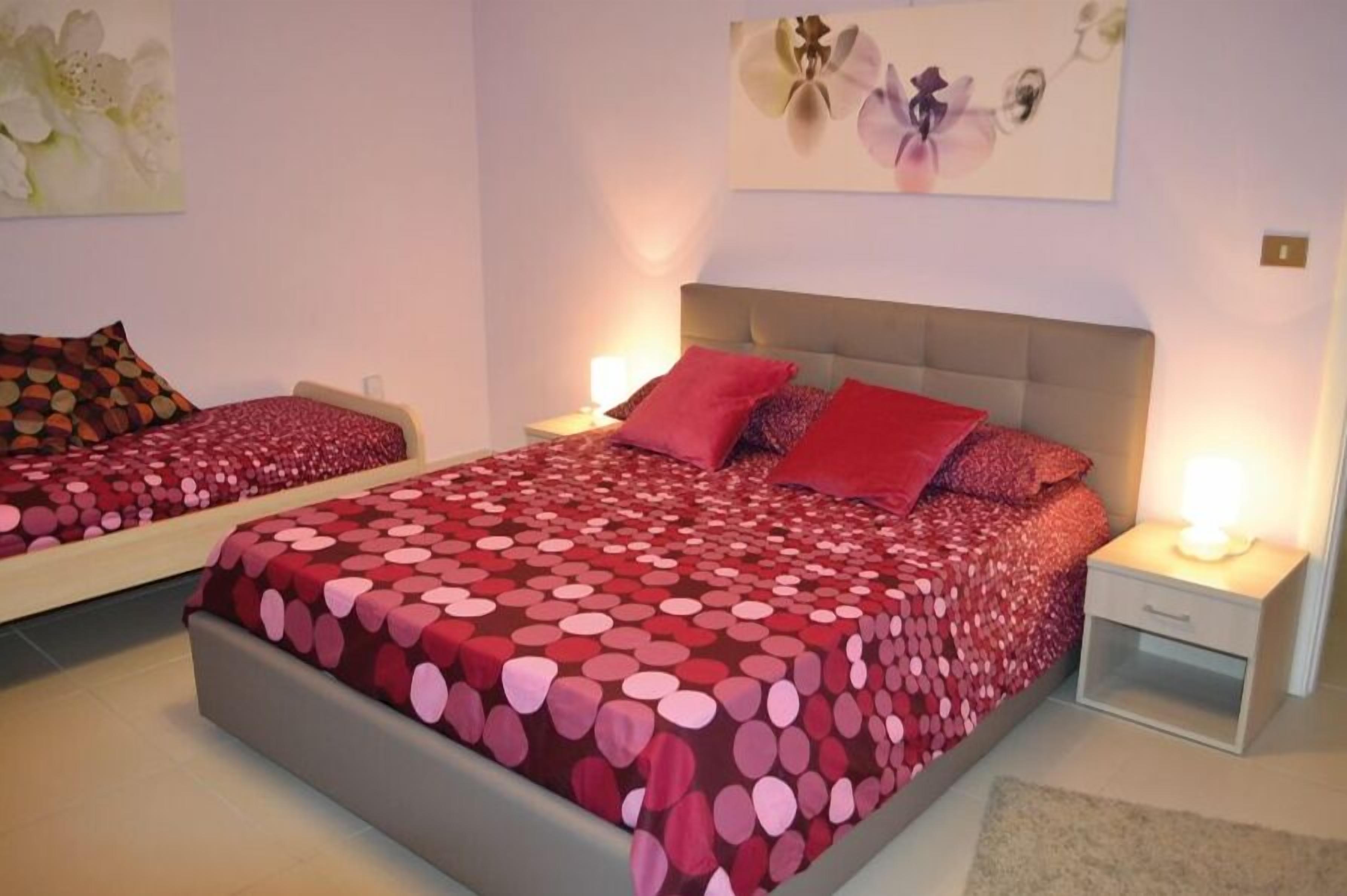 Camera da letto con due letti, ognuno con copriletto a pois rossi e bianchi, una testiera grigia e un comodino con una lampada.