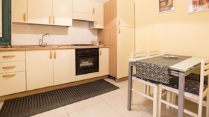 A compact kitchen with white cabinets, a built-in oven, and a dining area with a table and chairs. - B&B Monica's House (Salerno)