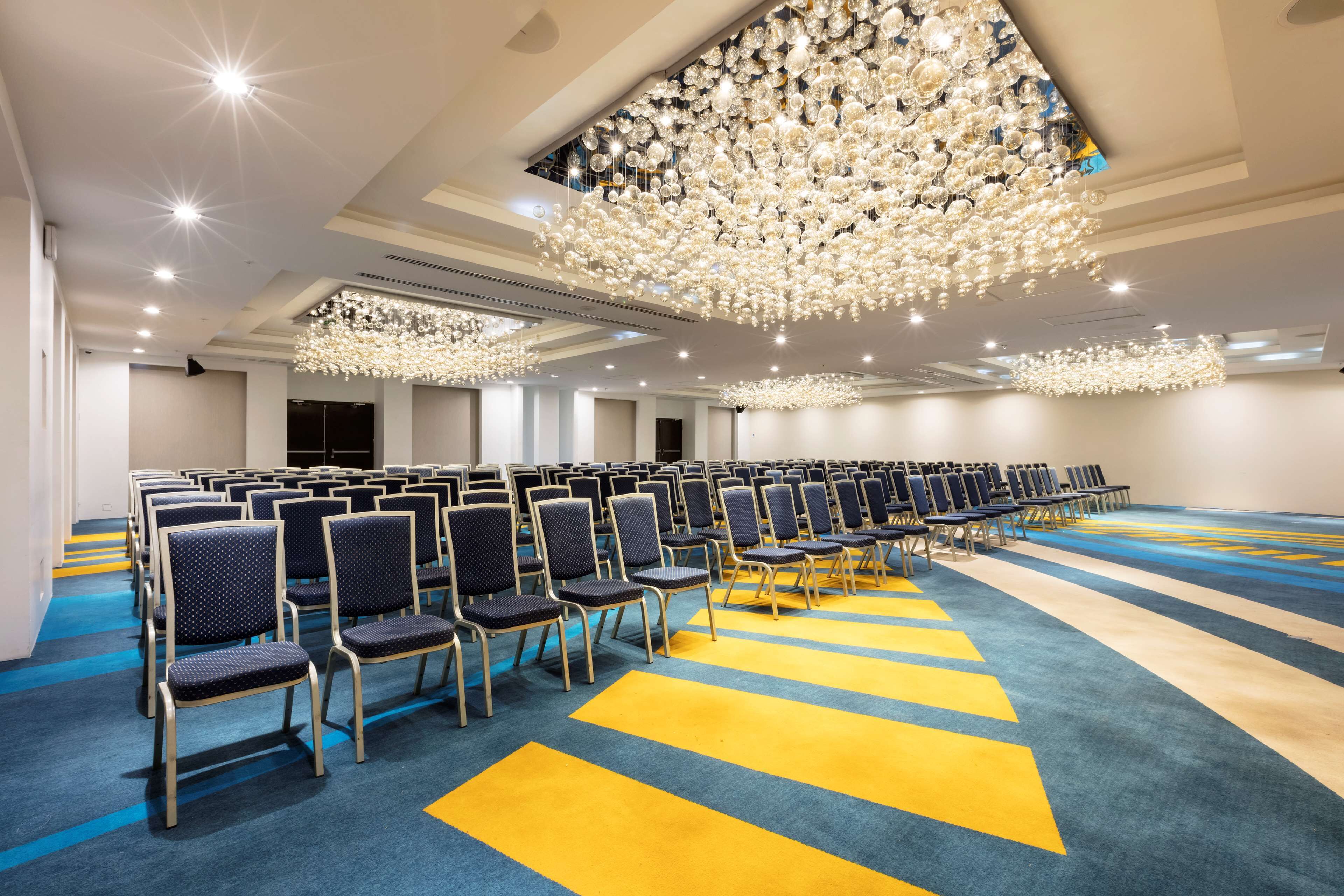 A conference room with rows of chairs, a patterned carpet, and a large chandelier.