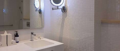 A bathroom with a white sink, two mirrors, and a handheld showerhead.