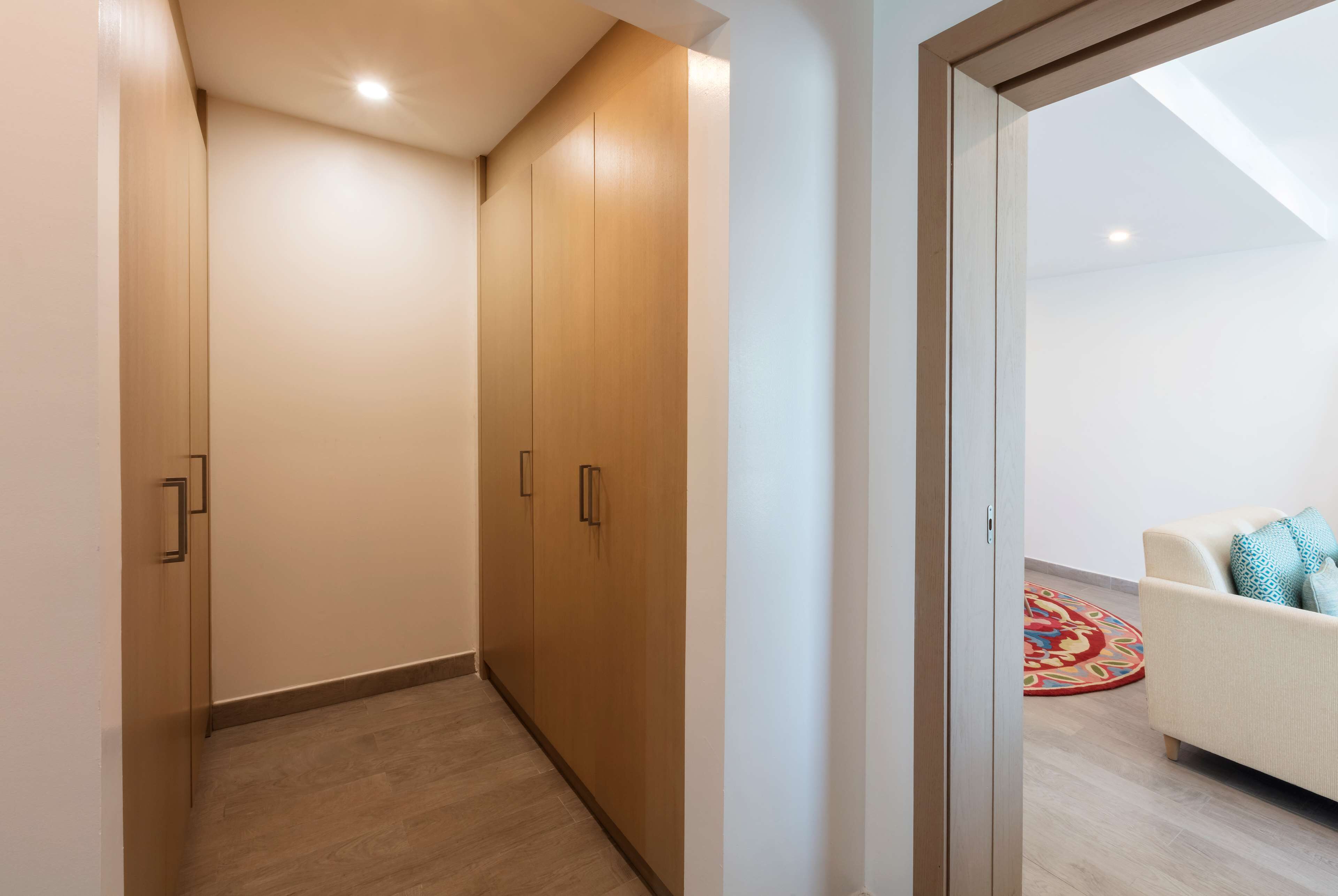 A hallway with wooden wardrobes, a white sofa with patterned cushions, and a colorful rug.