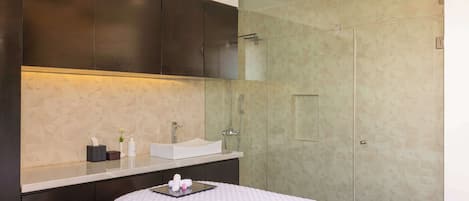 Un baño moderno con un espejo grande, cabina de ducha de vidrio y lavamanos blanco.