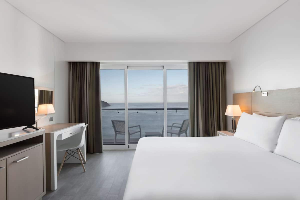 Una habitación de hotel con cama, escritorio, televisión y vista al mar.