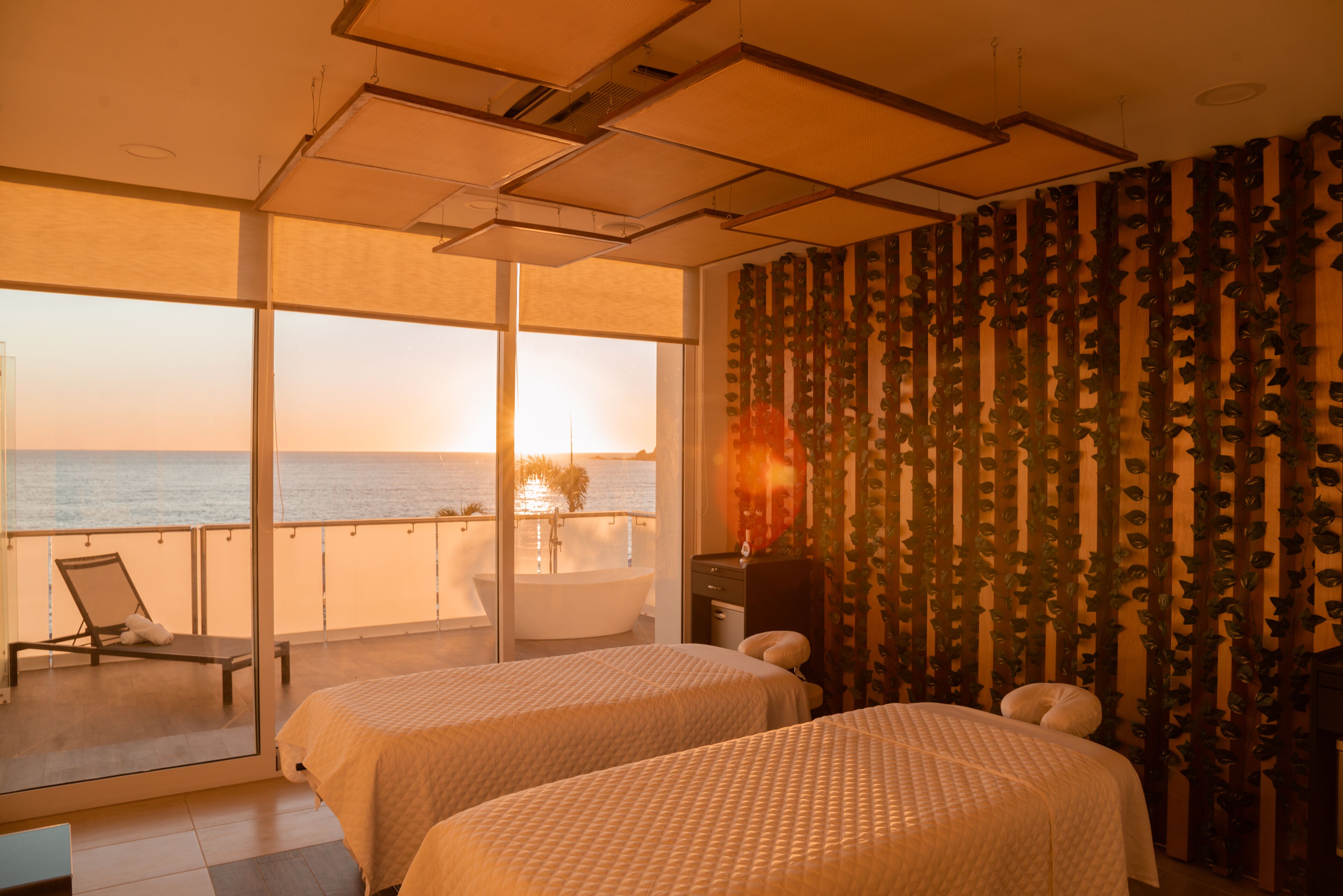 A hotel room with two beds, a balcony with a view of the sea, and a large window.
