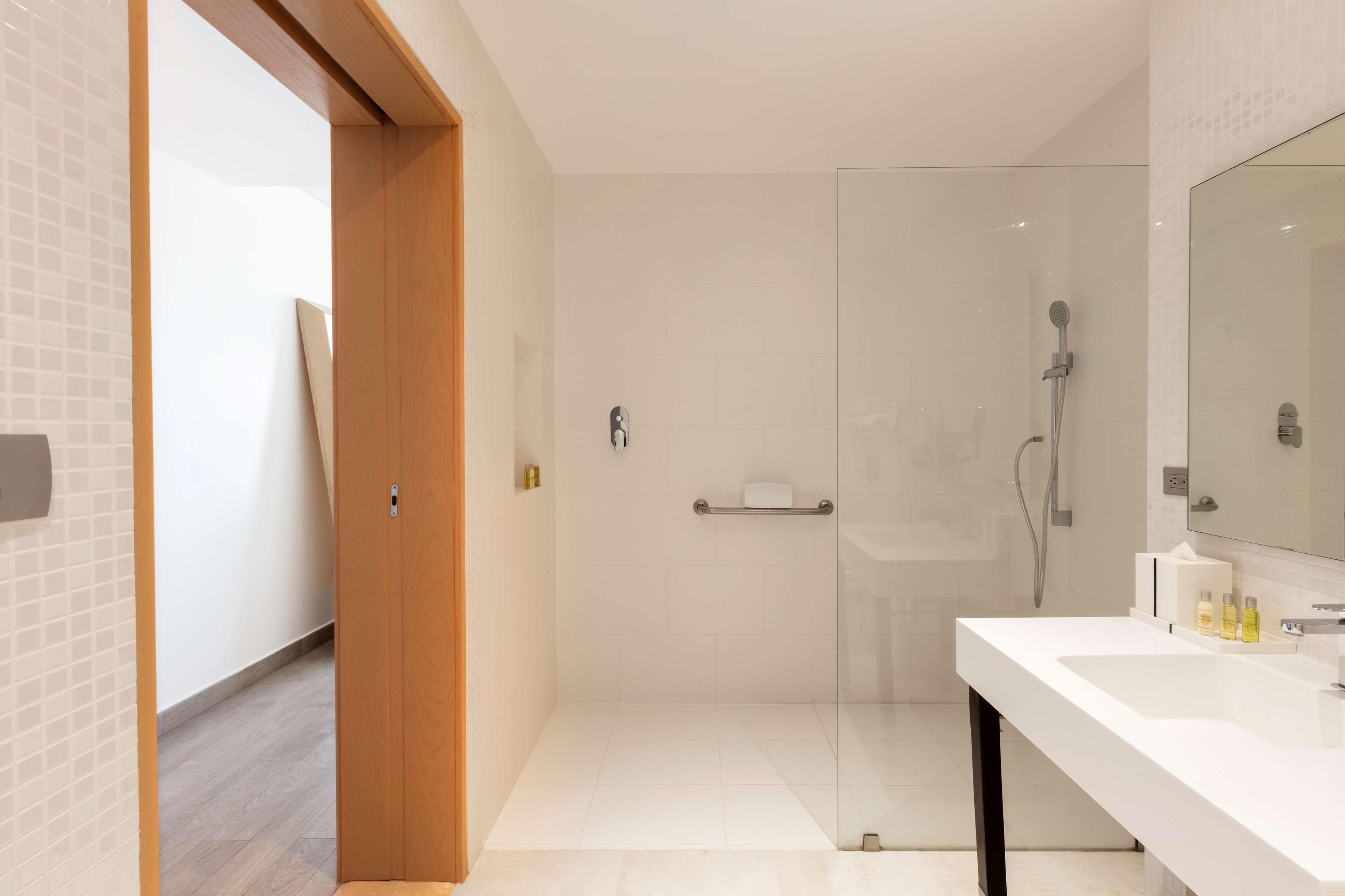 A modern bathroom with a glass shower enclosure, a white sink, and a wooden door.