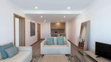 Un salon moderne avec un canapé, une table basse, un téléviseur et un coin cuisine à l’arrière-plan.