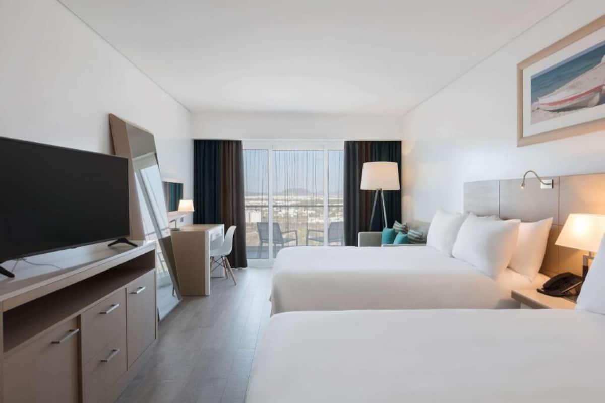 Habitación de hotel con dos camas, un escritorio, televisión y vistas a la ciudad.