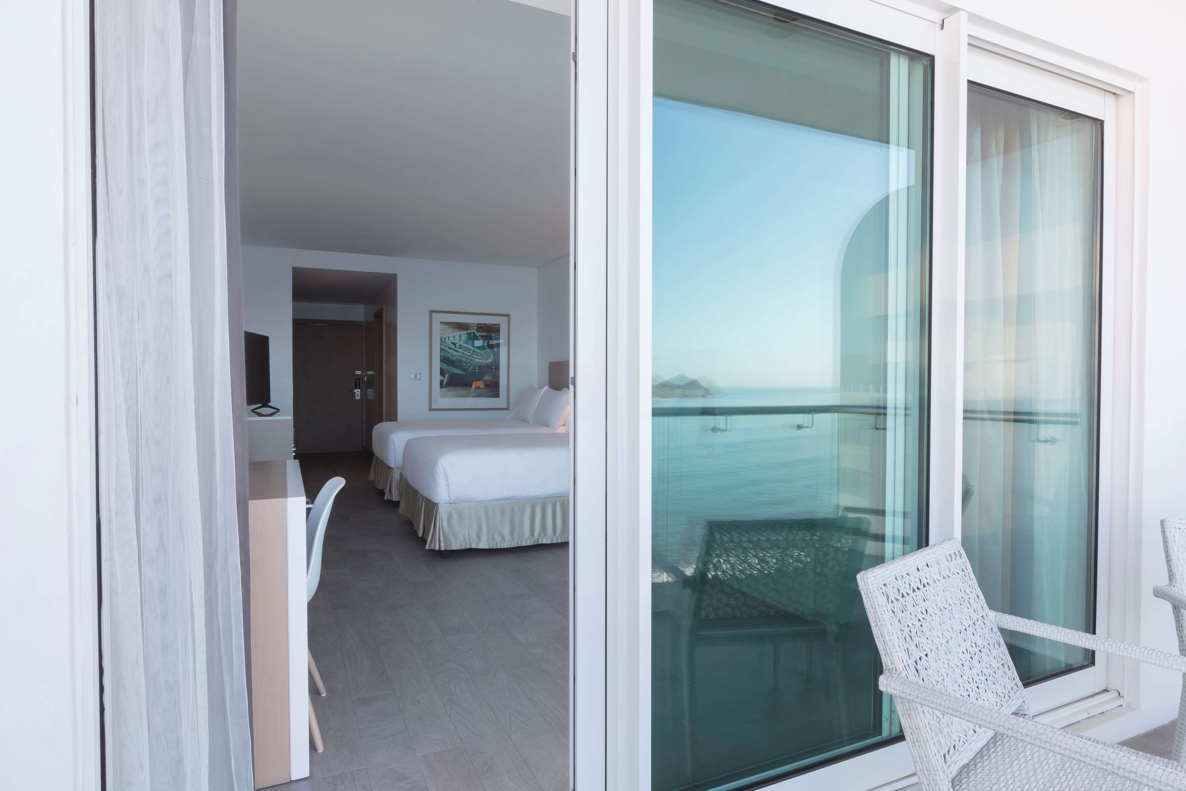 Habitación de hotel con balcón, dos camas, un escritorio y una silla.