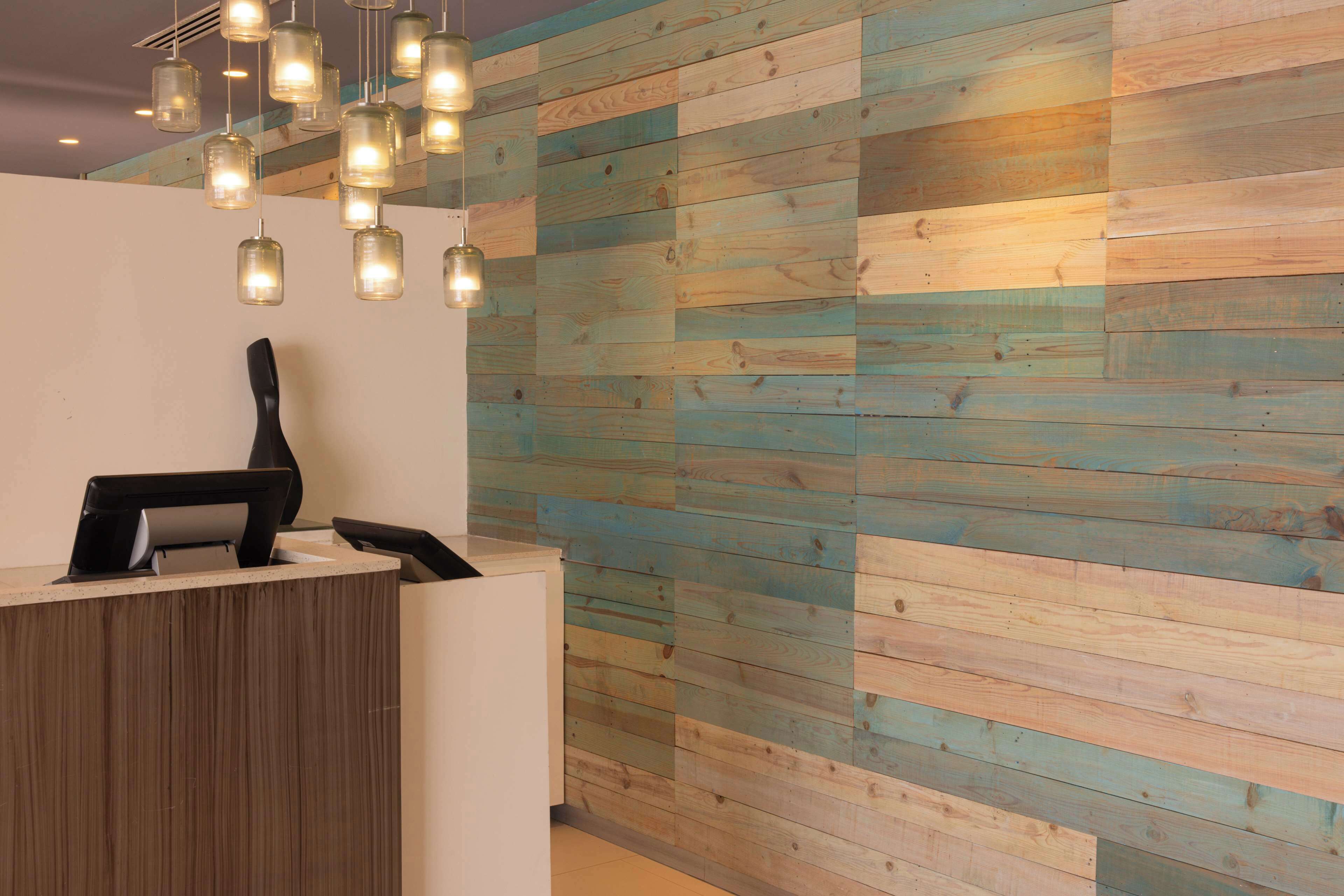Un área de recepción con pared de madera, mostrador de recepción e iluminación colgante.