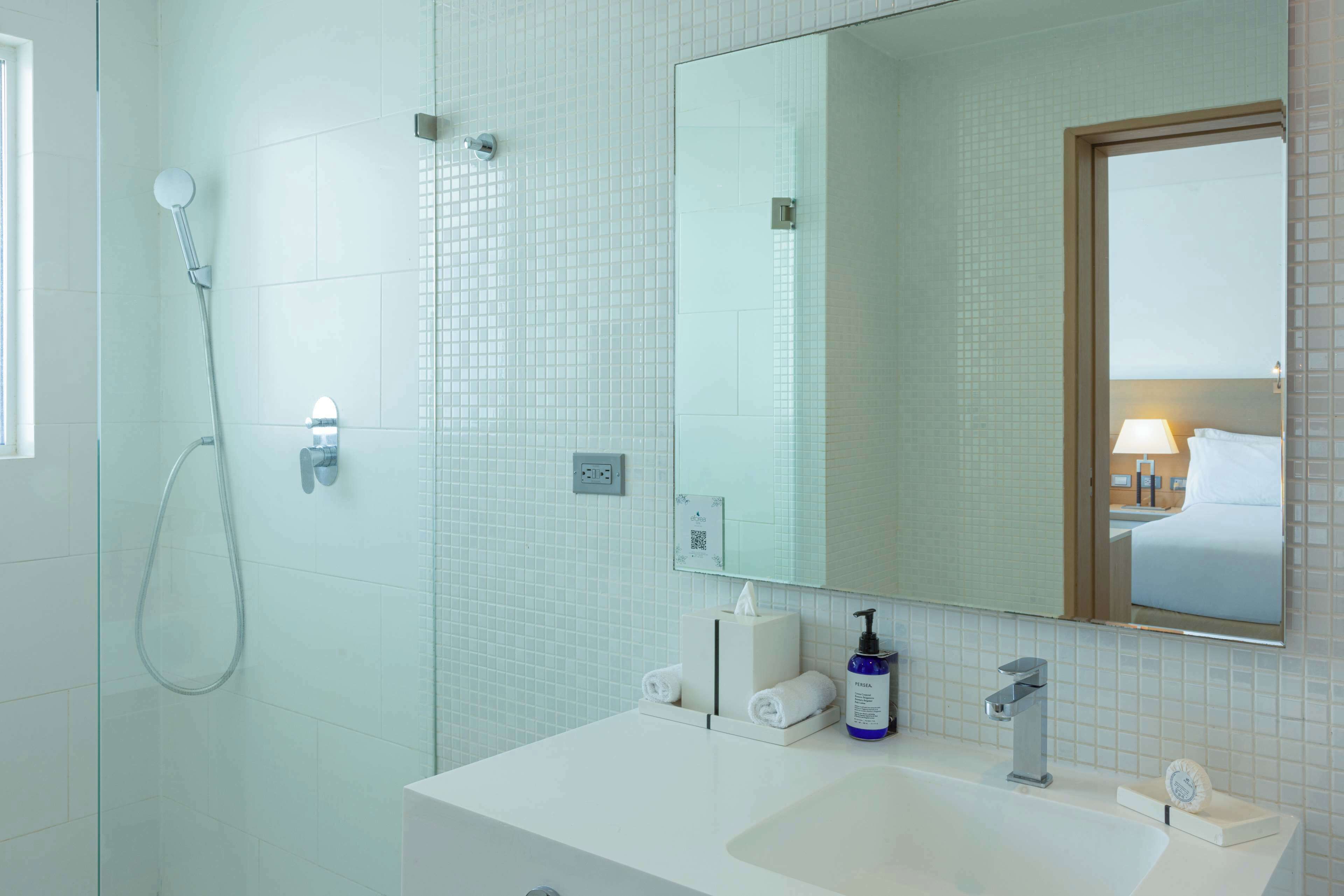 Un baño moderno con ducha de vidrio, lavamanos blanco y un espejo grande.