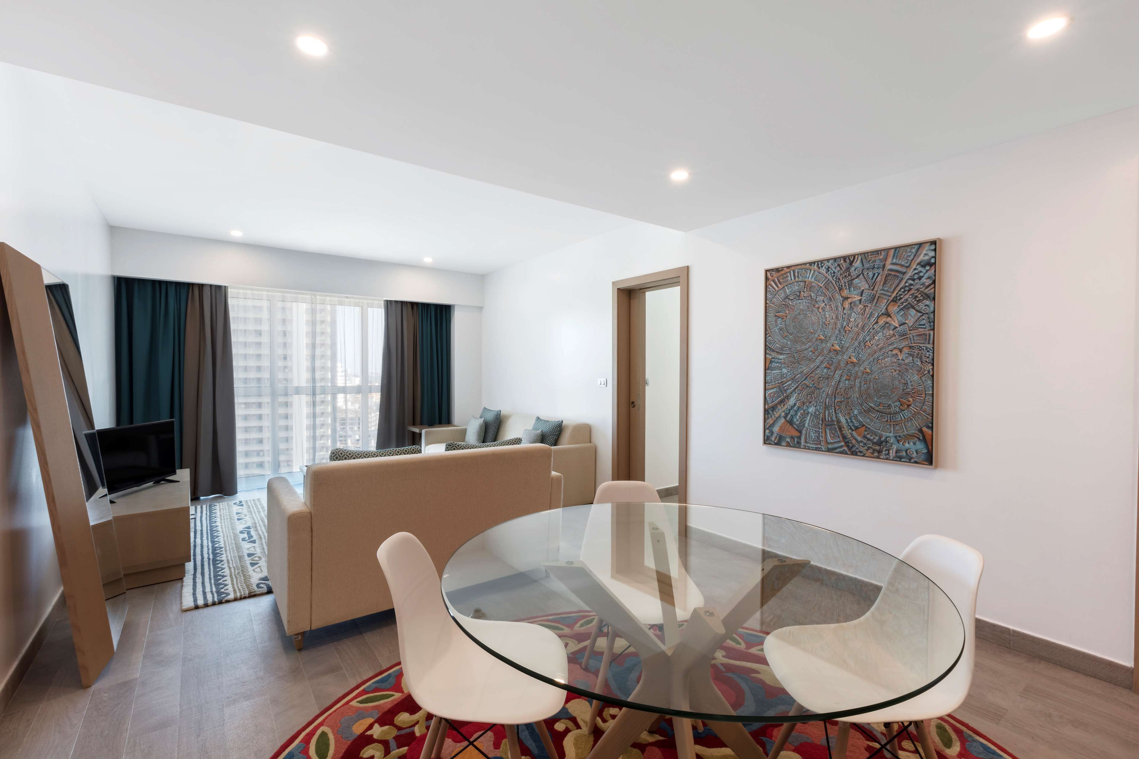 Una sala de estar moderna con una mesa de vidrio, un sofá color crema y un cuadro abstracto grande en la pared.