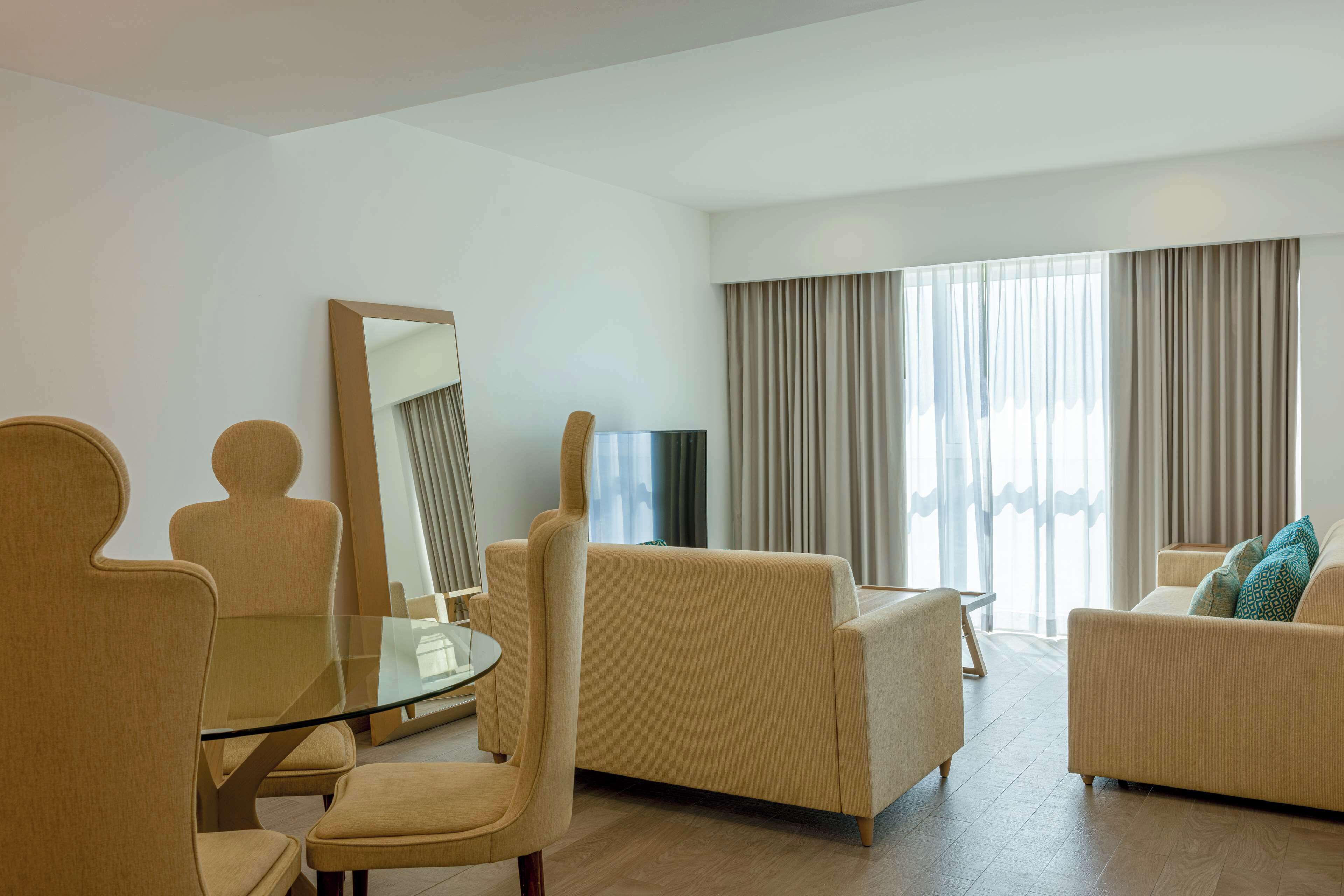 Una sala de estar moderna con una mesa de vidrio, sofás color beige y un espejo grande.