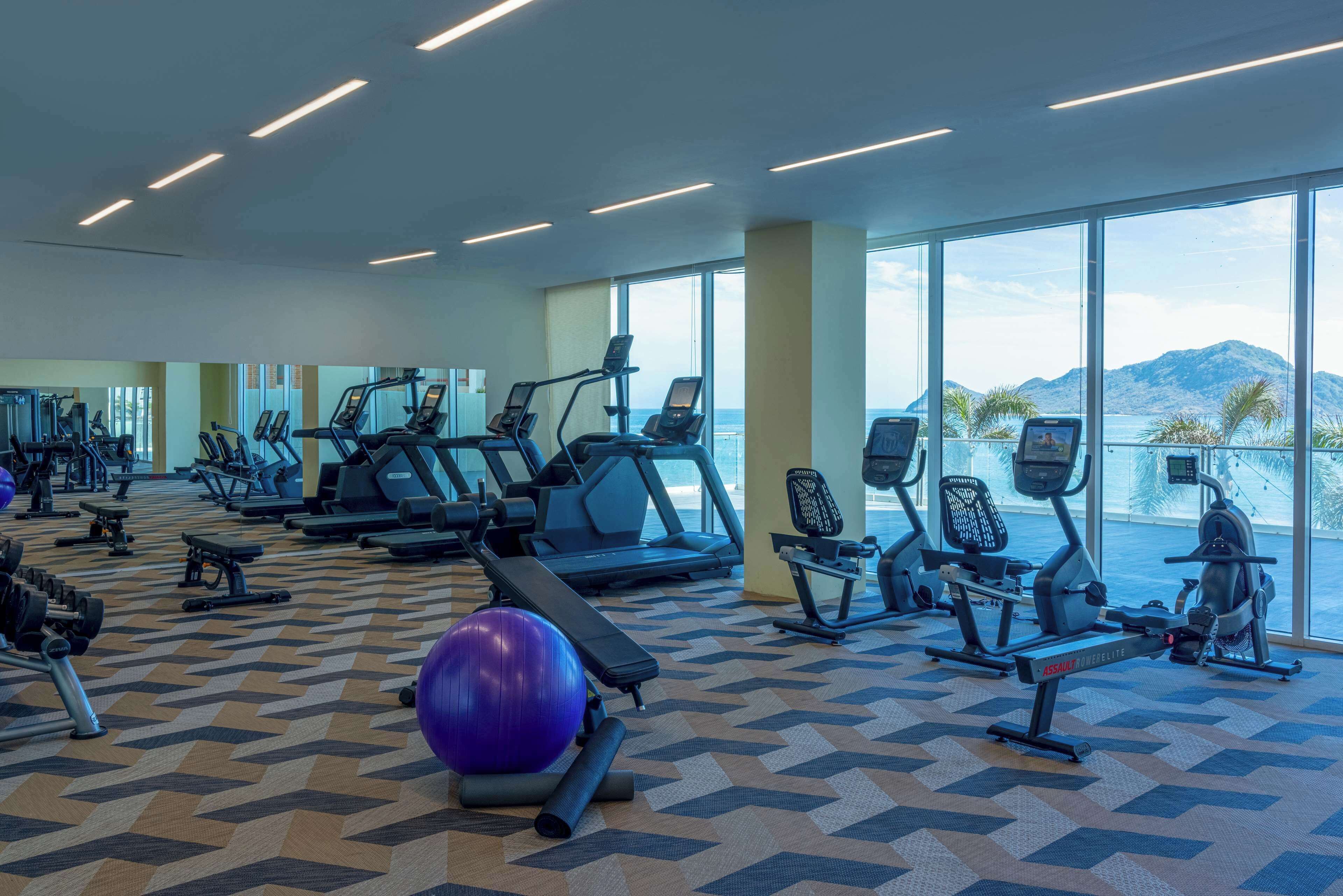 A gym with various exercise equipment, large windows, and a view of mountains.