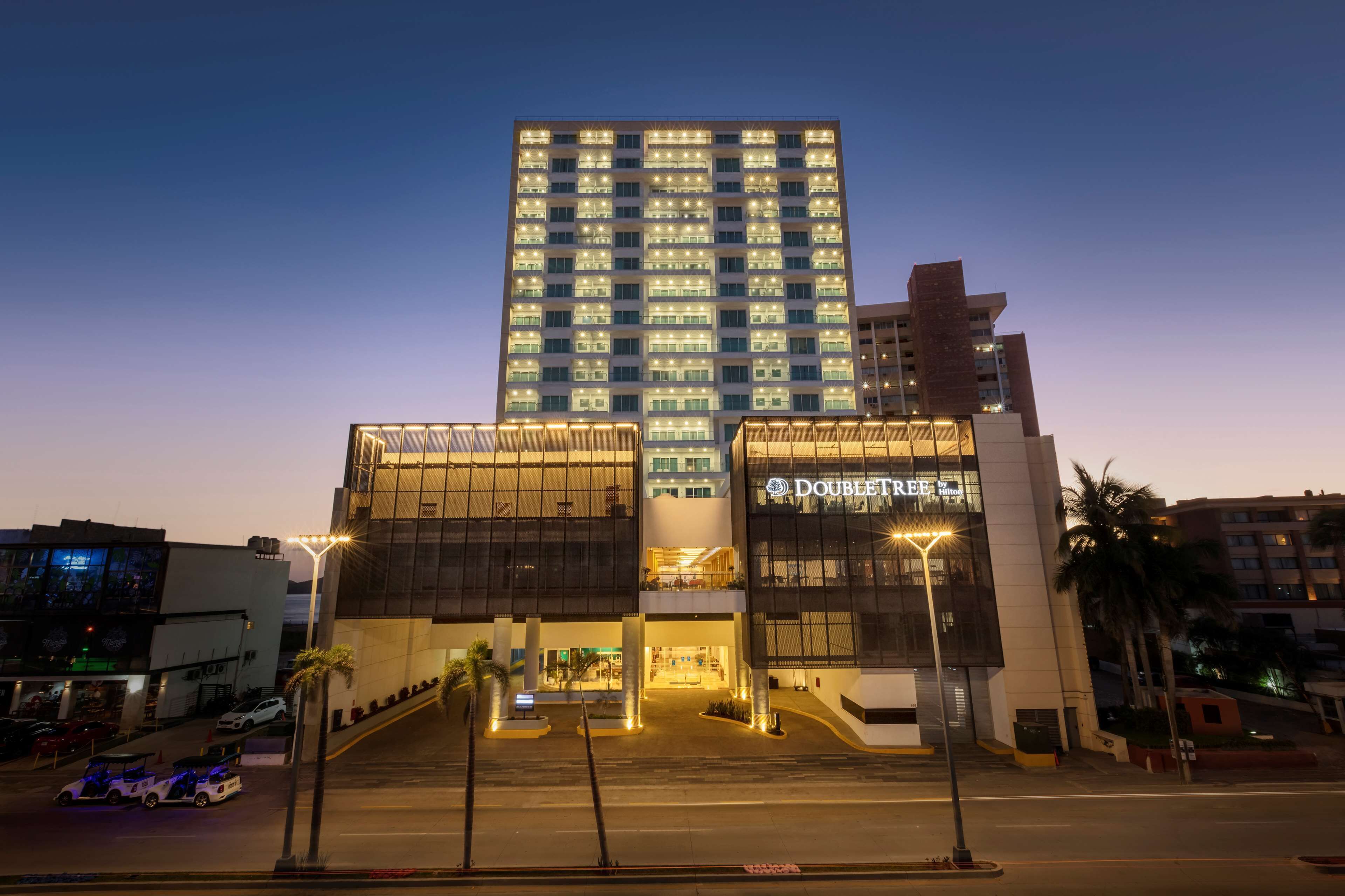 Un hôtel moderne doté d’une entrée imposante, de plusieurs étages et de fenêtres illuminées.