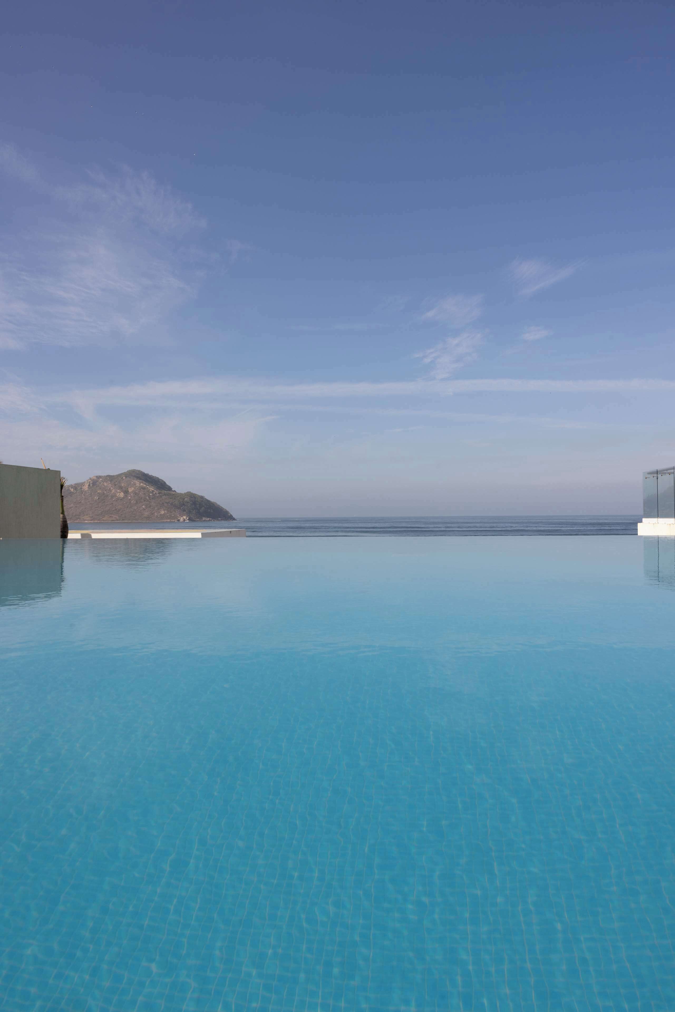A clear blue infinity pool with a view of the ocean and a distant mountain.