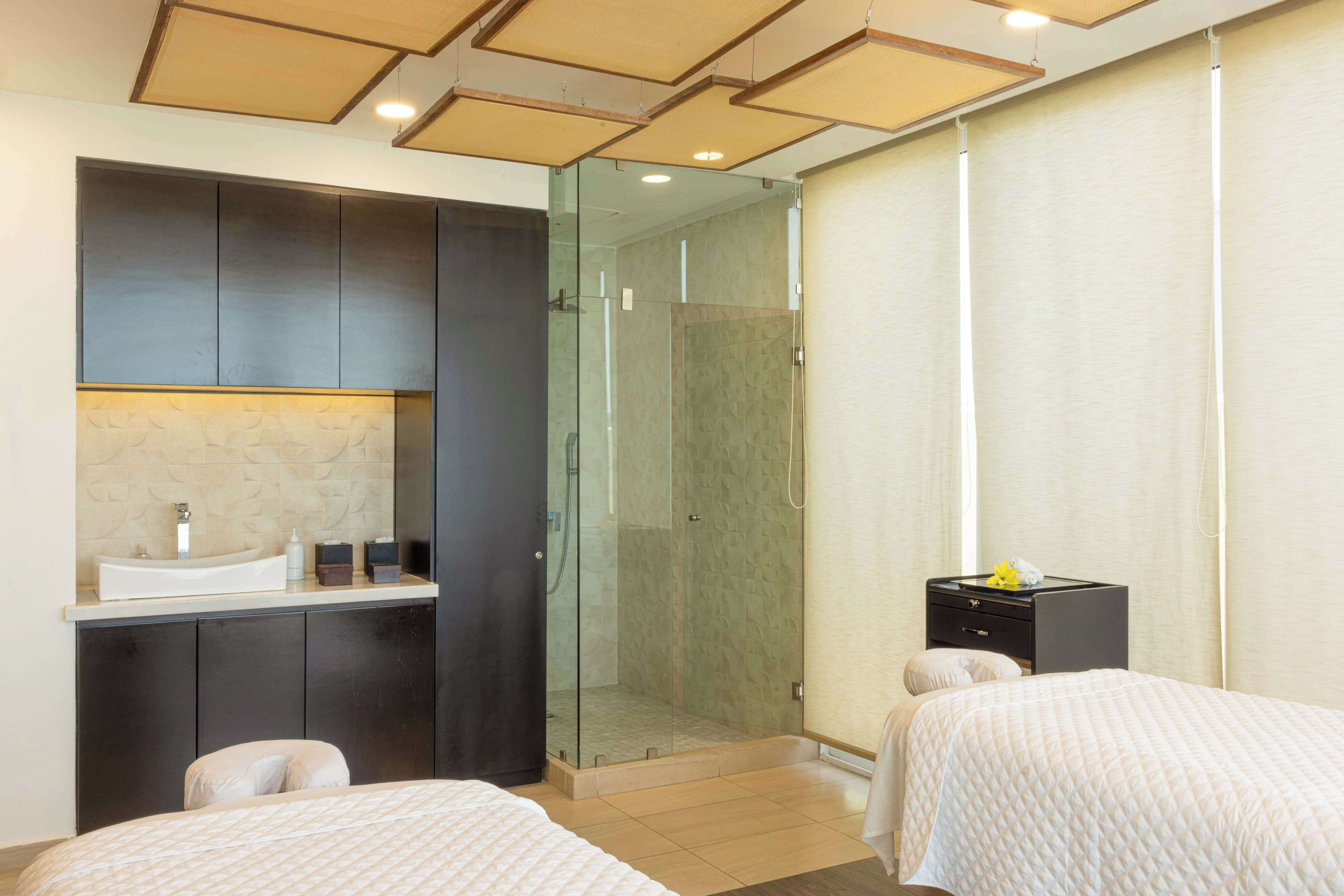 A hotel room with a bed, a small desk with a sink, a glass-enclosed shower, and a wardrobe.