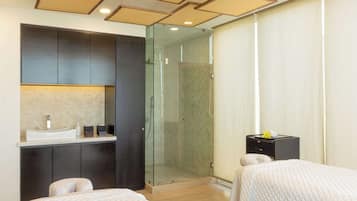 A hotel room with a bed, a small desk with a sink, a glass-enclosed shower, and a wardrobe.
