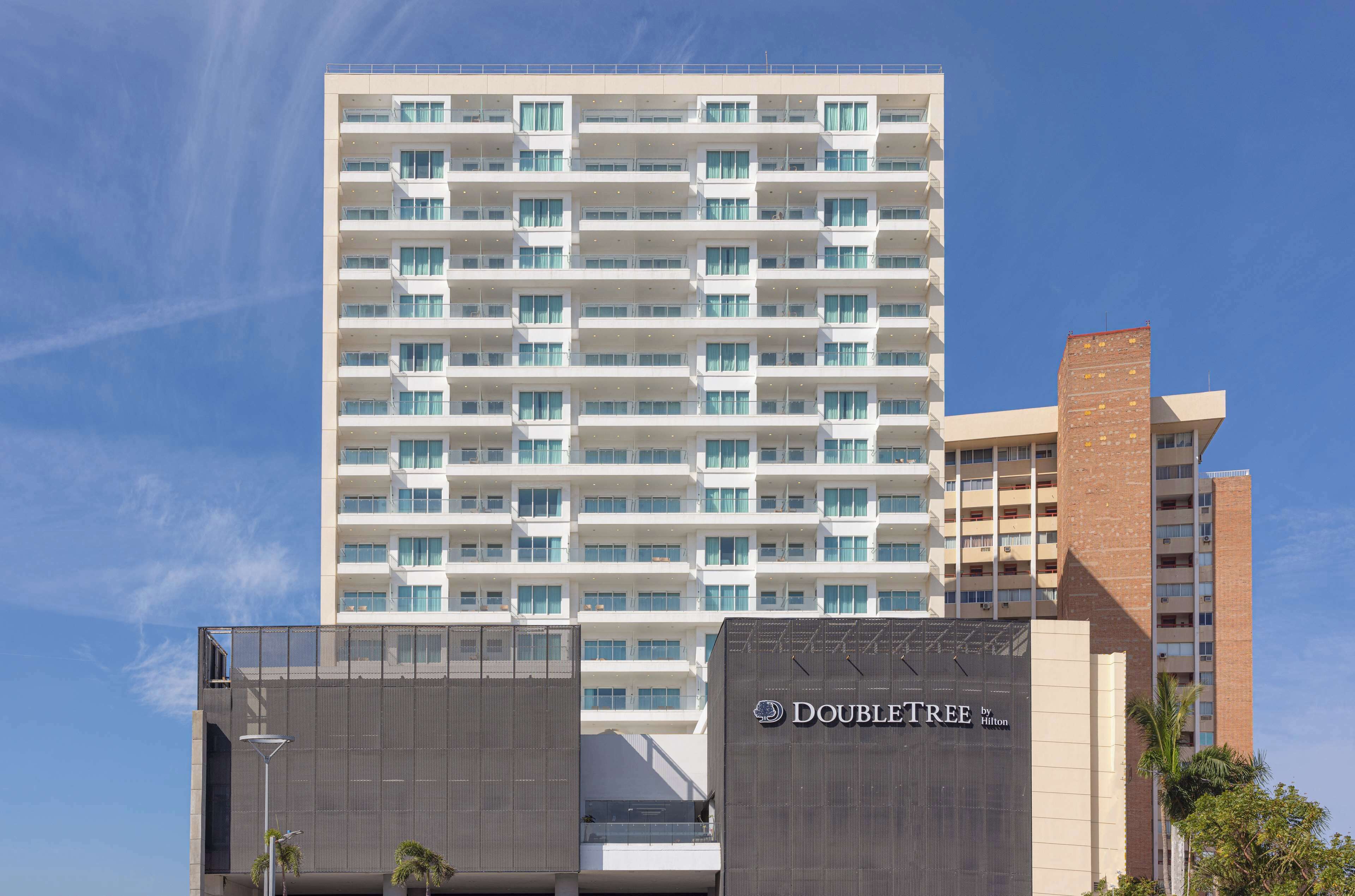 A modern hotel building with multiple floors, large windows, and a prominent "DOUBLETREE by Hilton" sign.