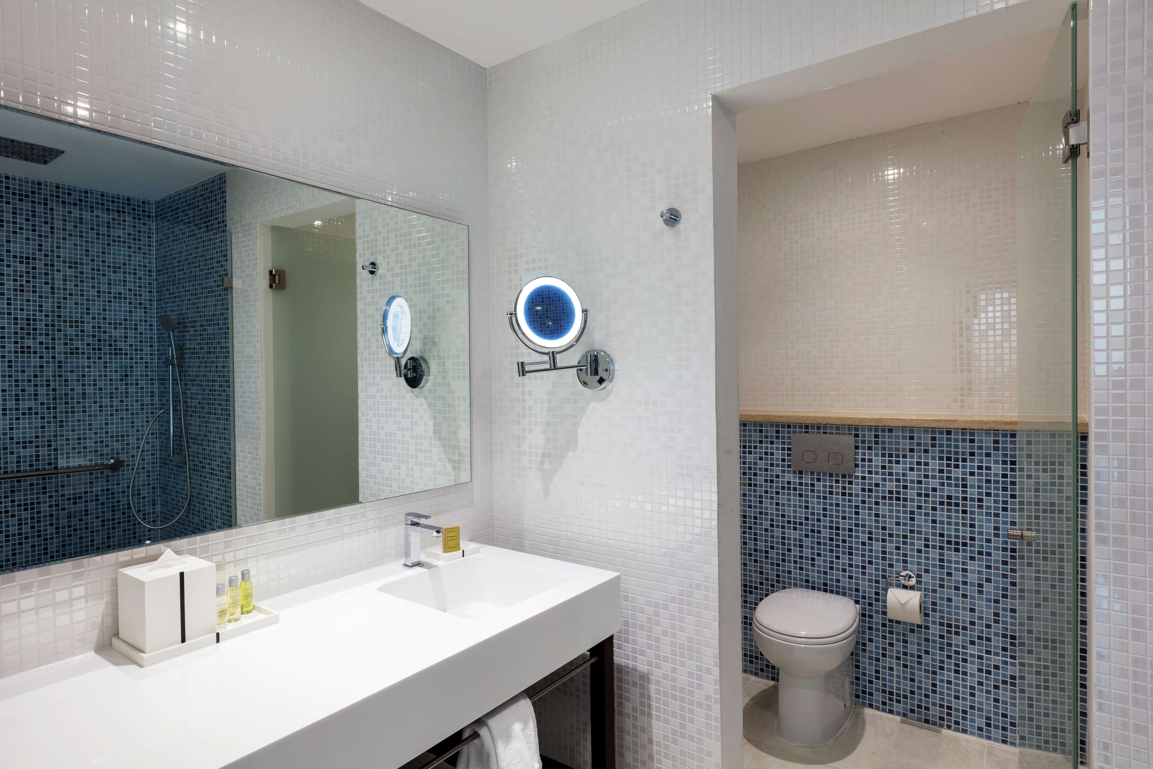 Un baño con lavamanos blanco, espejo, ducha de mano y retrete.