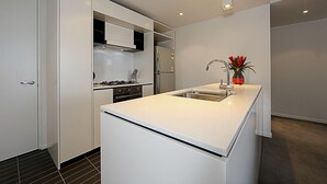 A modern kitchen with white cabinetry, a central island, and a stainless steel sink. - Accommodate Canberra - Dockside (Kingston)