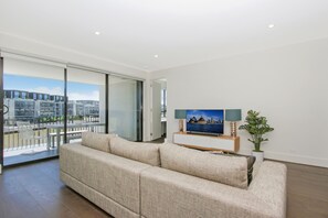 Una sala de estar moderna con un sofá grande, un televisor de pantalla plana y un balcón con vista a la ciudad.