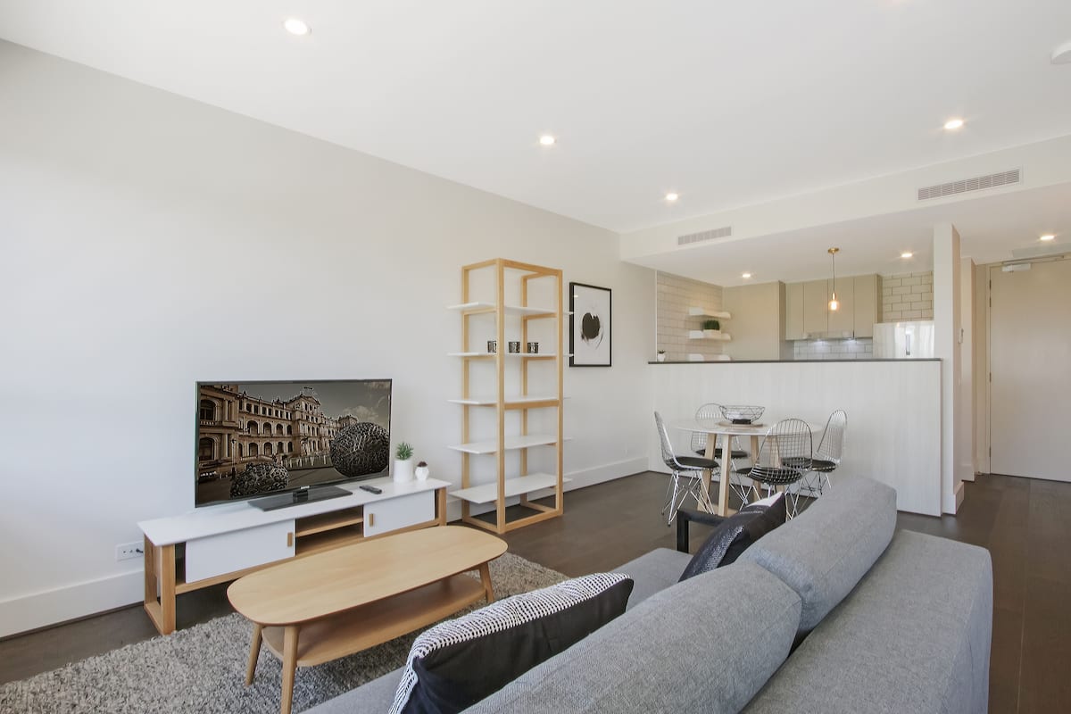 A modern living room with a sofa, coffee table, TV, and a dining area with chairs and a table.