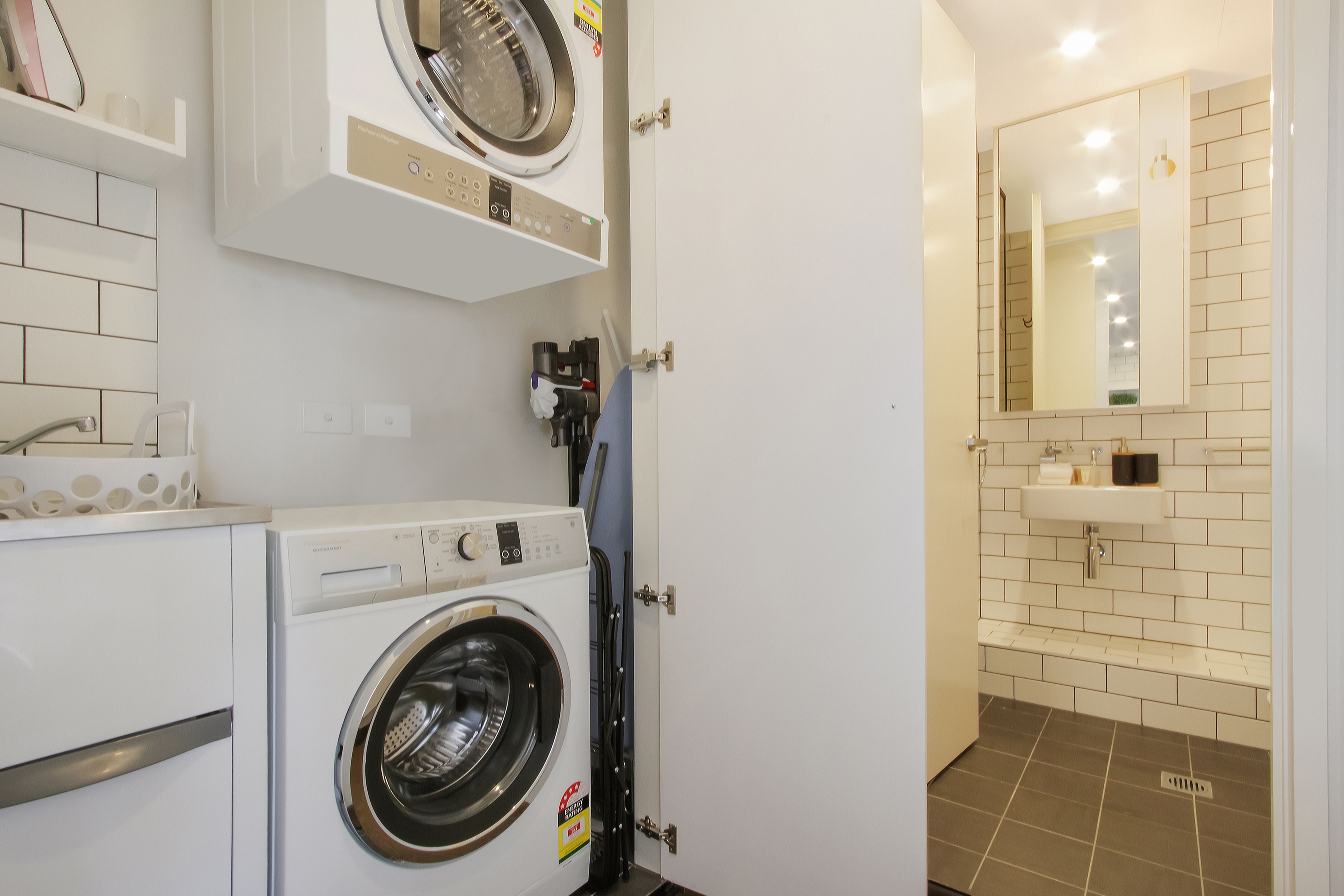 Een wasserette met een wasmachine, een droogmachine en een bijkeuken met een wasbak en spiegel.