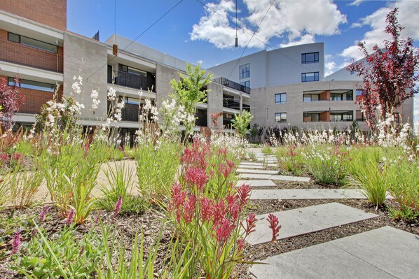 Un edificio moderno con varios pisos, zonas de estar al aire libre y un jardín con diversas plantas.