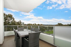 A balcony with a table and chairs, offering a view of a green landscape and a clear sky.