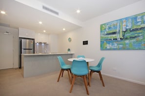 A modern kitchen with a central island, a dining area with four chairs, and a large abstract painting on the wall.