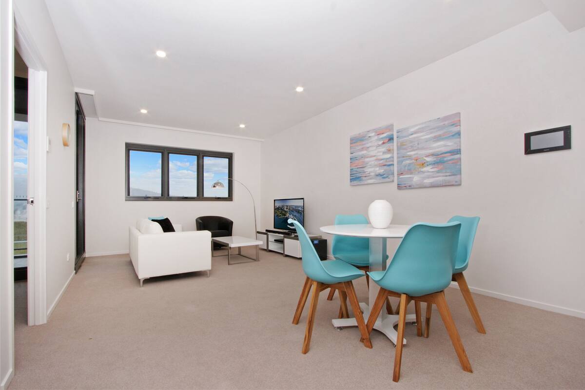 A modern living room with a white sofa, a dining table with blue chairs, and artwork on the walls.