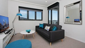 Uma sala de estar moderna com um sofá cinzento, uma mesa de centro branca, um abajur azul e um espelho grande na parede.