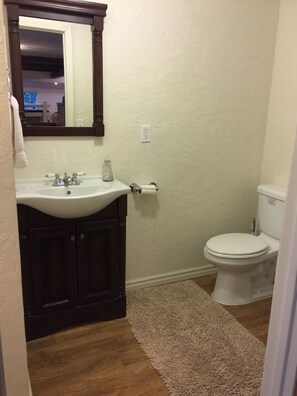 A bathroom with a wooden vanity, a white sink, a mirror, a toilet, and a beige rug. - Treetop Cabin (Auberry)