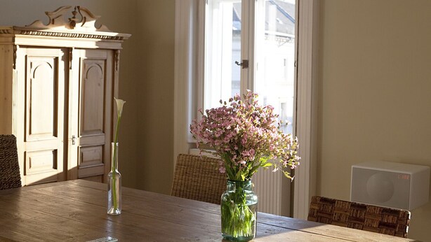 A dining table with a vase of flowers and a tall vase with a single flower.