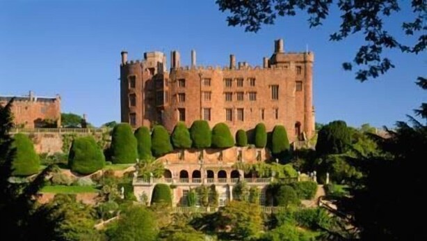 A historic castle with a large central tower, surrounded by well-manicured gardens and a formal courtyard.