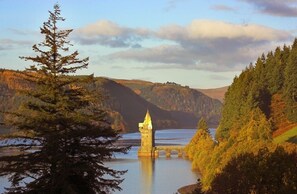 Une tour se dressant sur un lac, entourée de collines boisées.