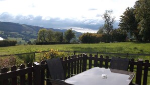 A patio with a table and chairs, overlooking a green landscape with hills and trees.