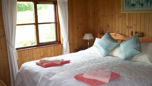 A wooden room with a bed, two pillows, and a window with curtains.