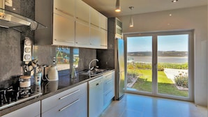 A modern kitchen with a stainless steel refrigerator, a built-in oven, and a large window offering a view of a landscaped garden.