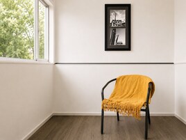 A room with a single chair, a framed picture on the wall, and a window with a view of trees.