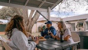 Un espacio al aire libre cubierto para comer, con una mesa, sillas, una botella de vino y una lata de cerveza.