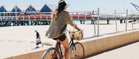Una persona pedaleando en bicicleta con una cesta por un sendero arenoso cerca de un muelle.