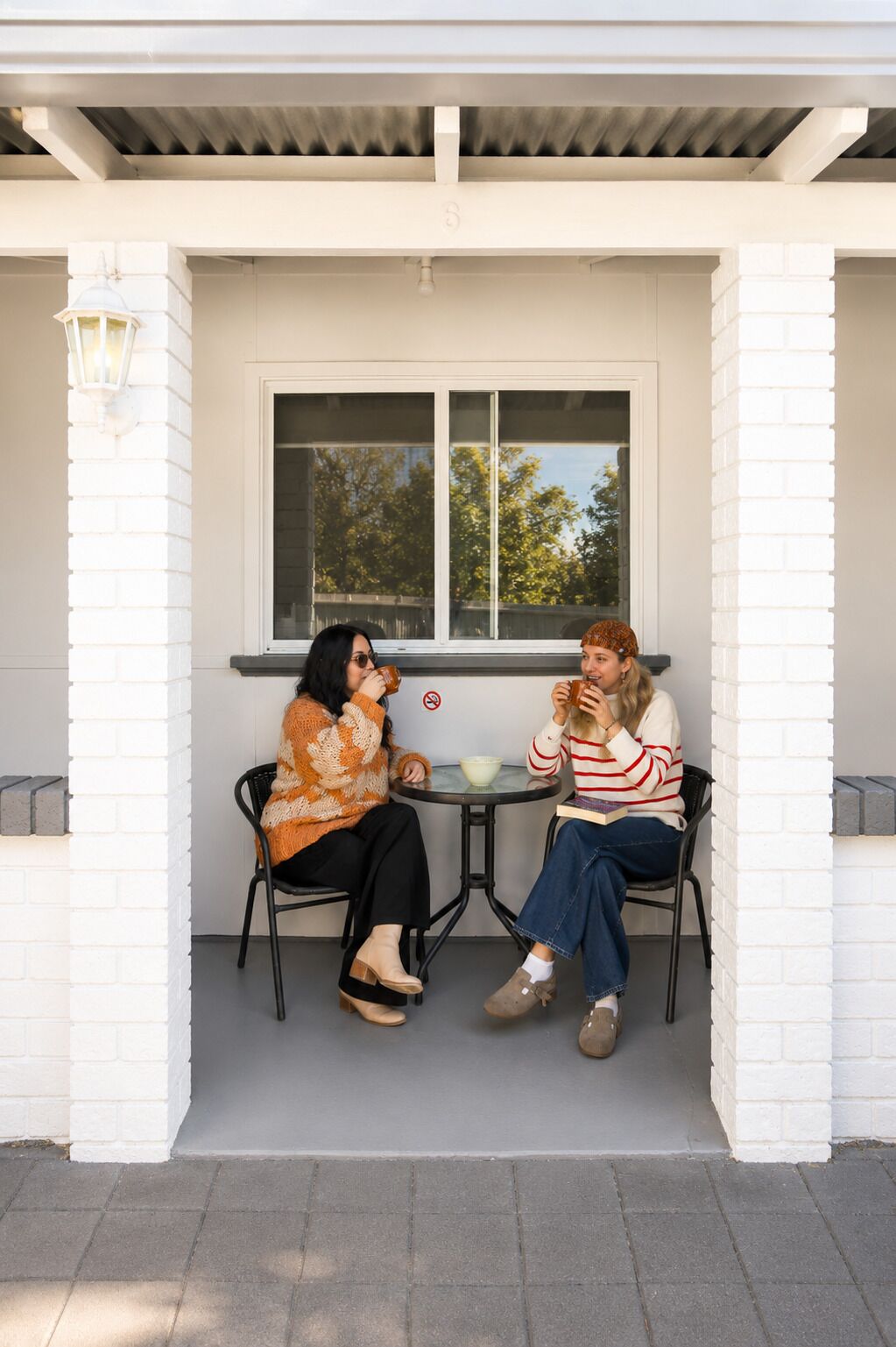 Two people sitting at a table on a porch with a window in the background.