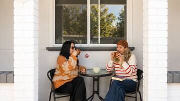 Two people sitting at a table on a porch with a window in the background.