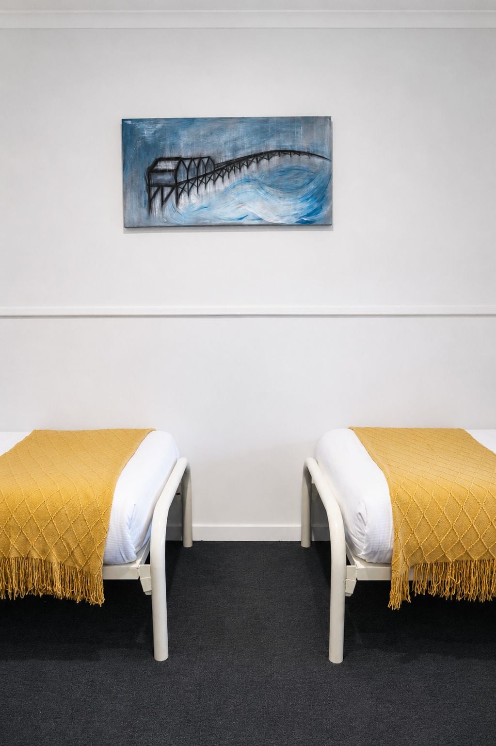Quarto com duas camas, um quadro na parede e piso coberto por carpete.