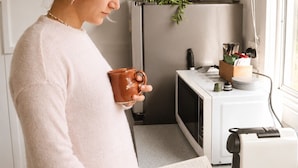 Una persona leyendo un libro en una cocina con un microondas, un lavabo y una ventana.