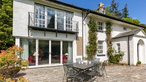 A two-story house with a patio area featuring a table and chairs, large sliding glass doors, and a balcony with a railing. - Magnificent Family House with Stunning Private Garden (Drymen)